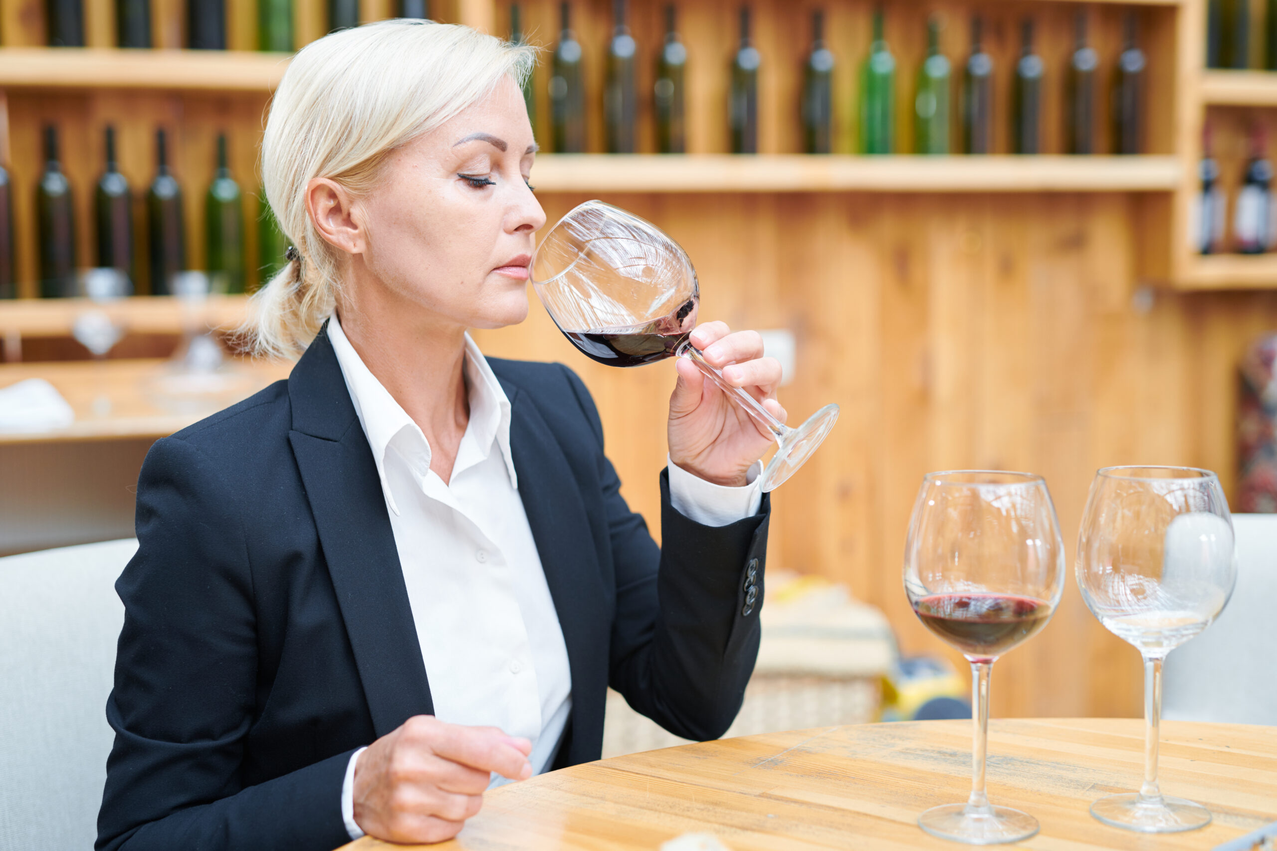 Elegant sommelier sitting by table in cellar and tasting cabernet from wineglass Elegant sommelier sitting by table in cellar and tasting cabernet from wineglass to check its quality