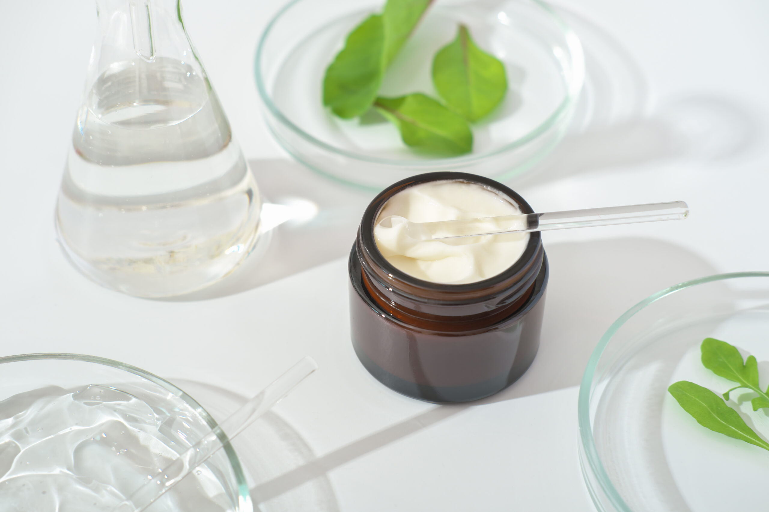 Cosmetic container with green herbal leaves and scientific glassware, Research and develop natural organic beauty skincare product, copy space, banner Cosmetic containers with green herbal leaves and scientific glassware, Research and develop natural organic beauty skincare product.